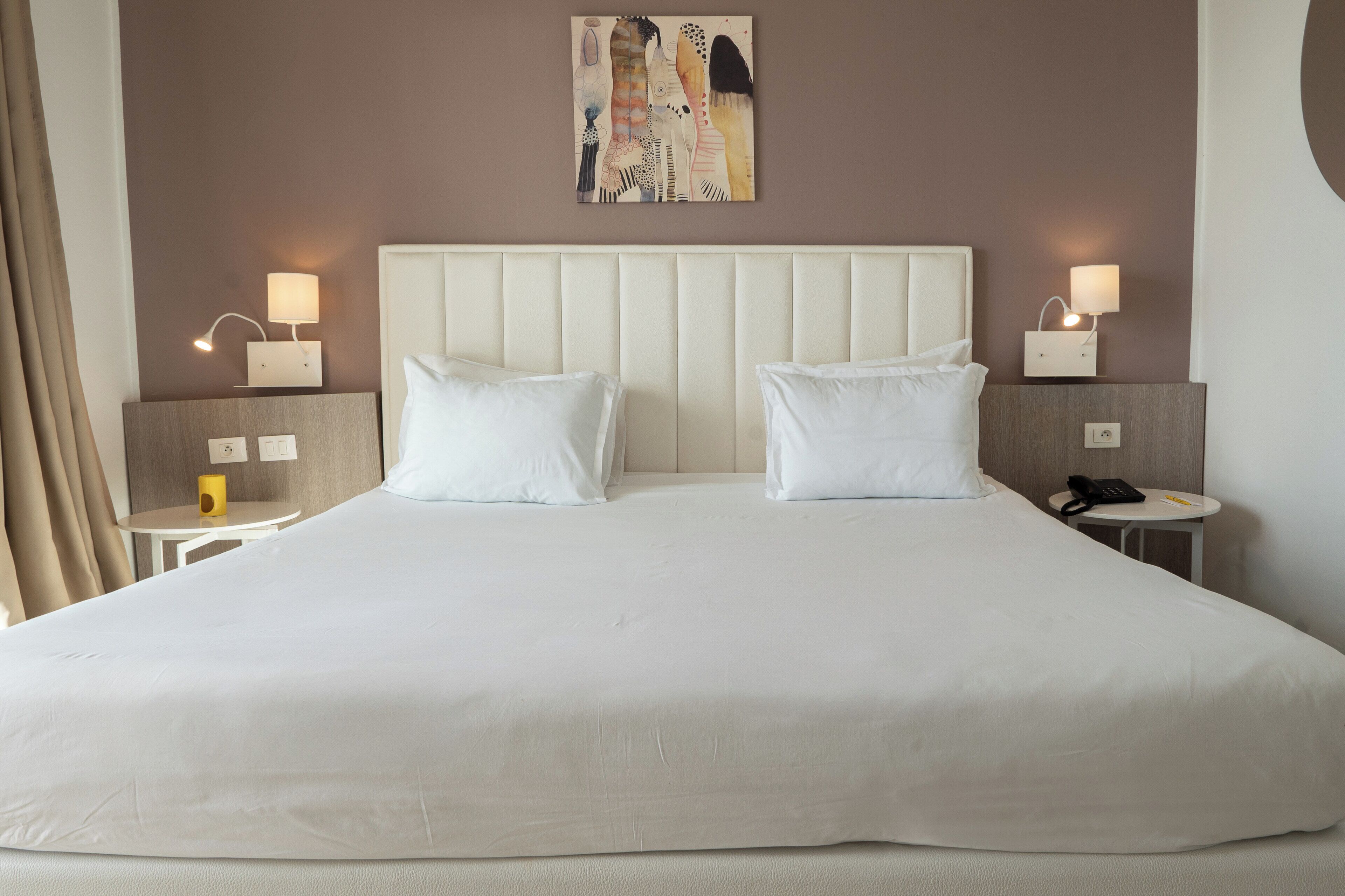 A large bed with two pillows, a headboard, bedside tables with lamps, a wall art piece, and a phone on one of the tables.