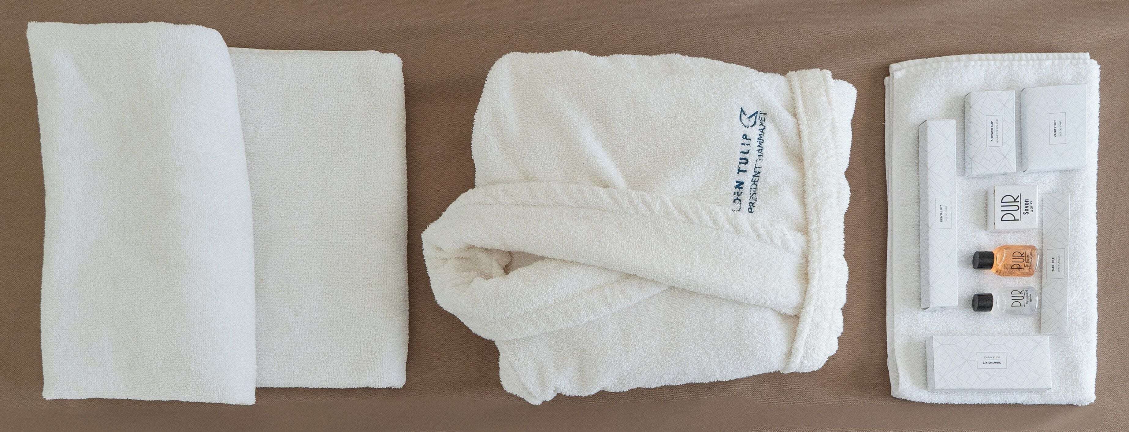 En prydligt vikt vit handduk, en ihopvikt handduk och ett set med toalettartiklar, inklusive en flaska PUR-schampo och balsam, en tvål och en tandborste.
