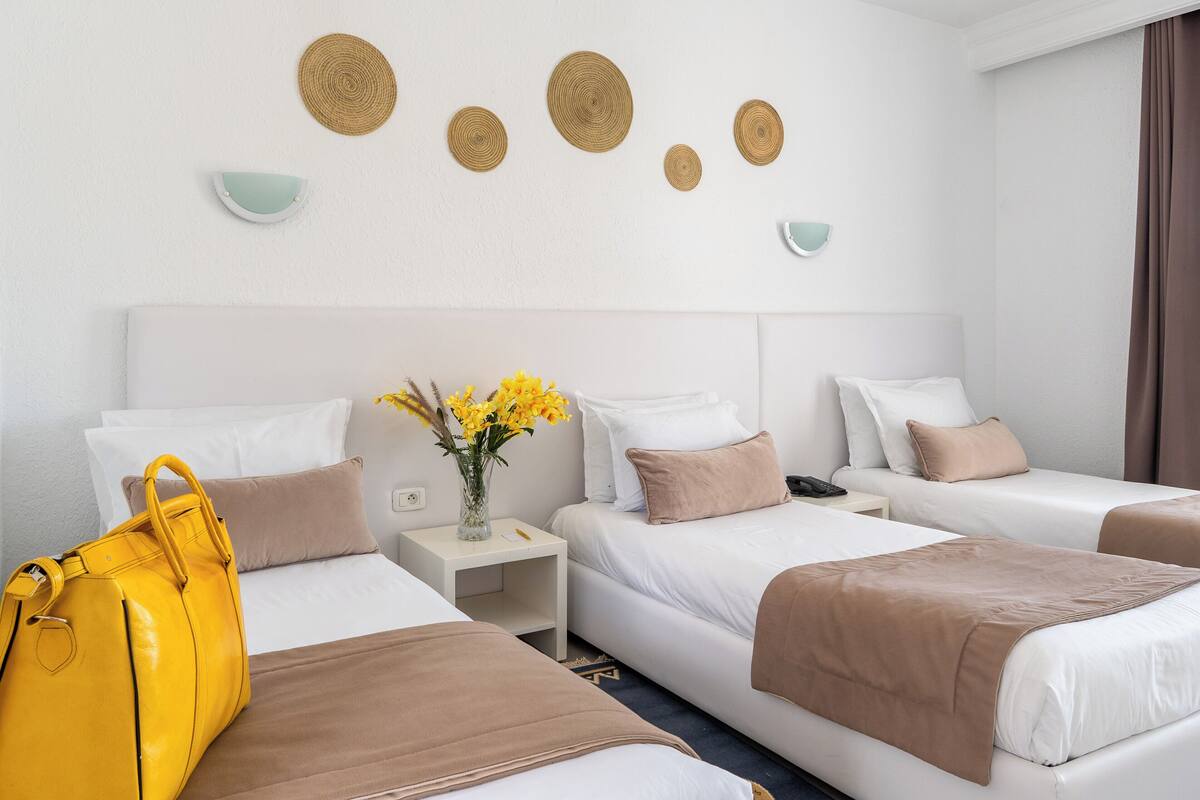 A hotel room with two beds, a nightstand, a yellow handbag, and decorative wall art.