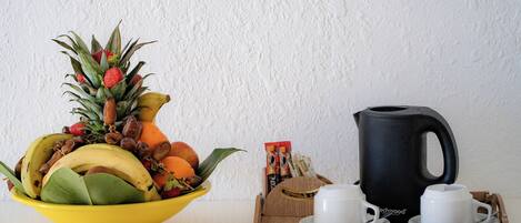 Un tazón amarillo con frutas y una cafetera negra sobre una bandeja con tazas.