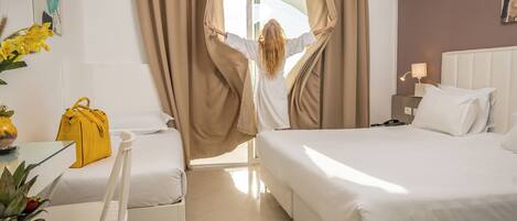 A hotel room with two beds, a dining table with a yellow bag, and a fruit basket.