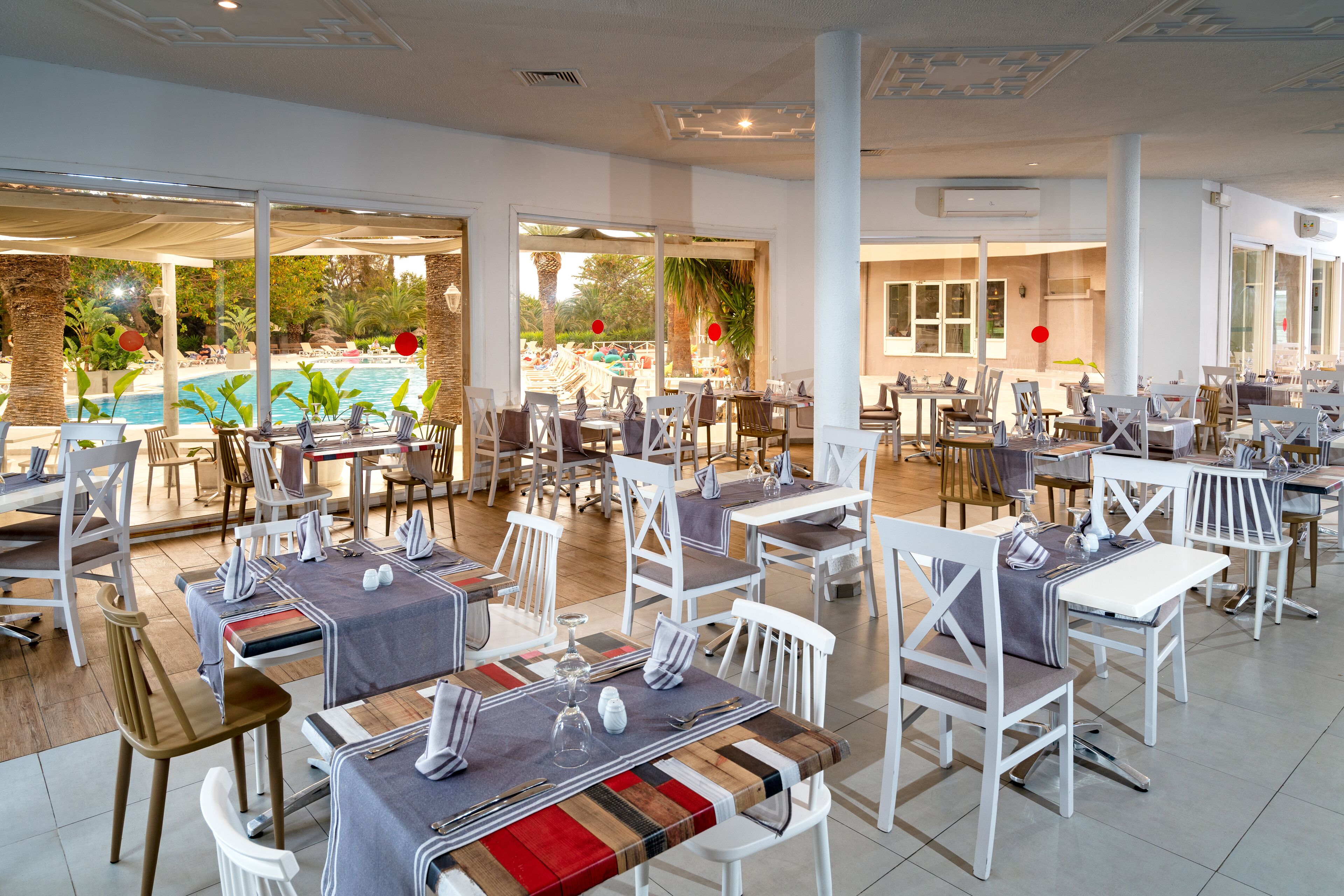 Un restaurante con terraza al aire libre y vistas a una piscina, con mobiliario blanco y un diseño moderno.