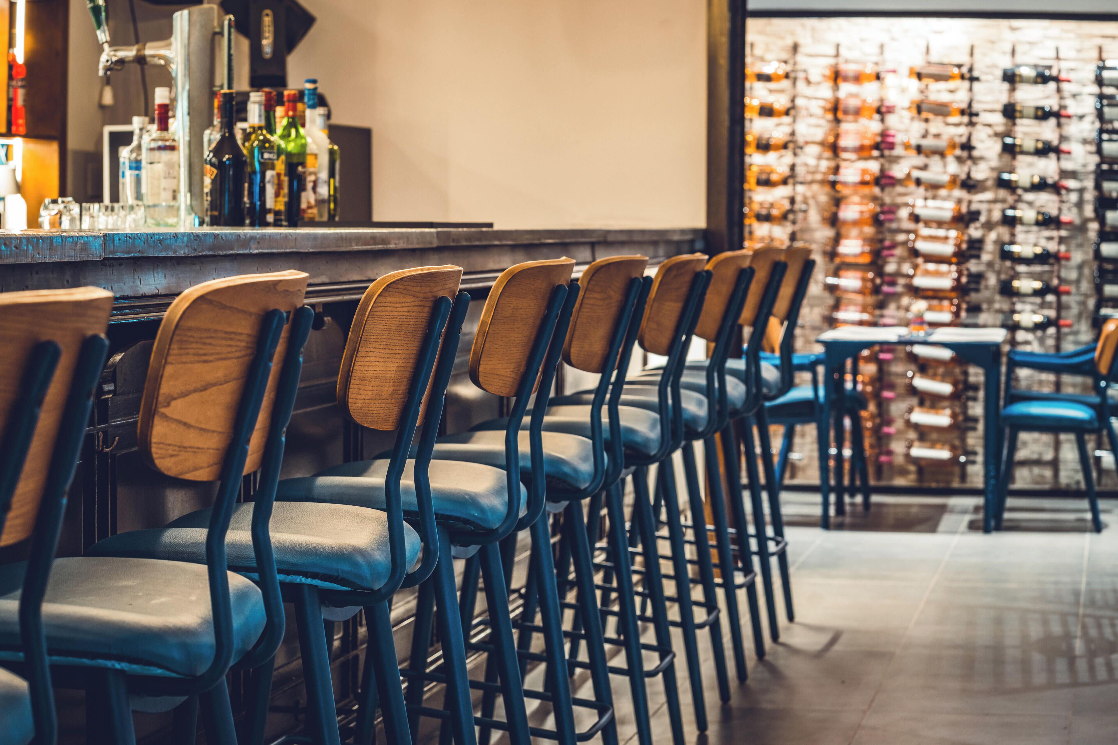 A bar area with rows of chairs and a wall of wine bottles.