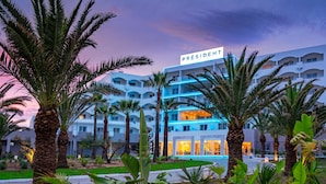 Un hôtel avec une enseigne indiquant  « Président », de nombreux étages et un espace piscine.