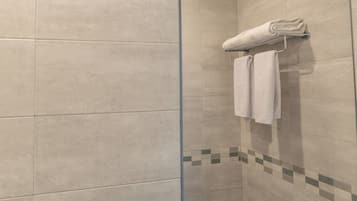 A bathroom with beige tiles, a glass shower door, and a towel rack with folded towels.