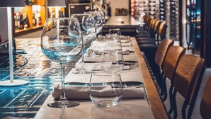 Una zona de bar con copas de vino y servilletas ordenadas sobre una mesa, y una barra con sillas al fondo.