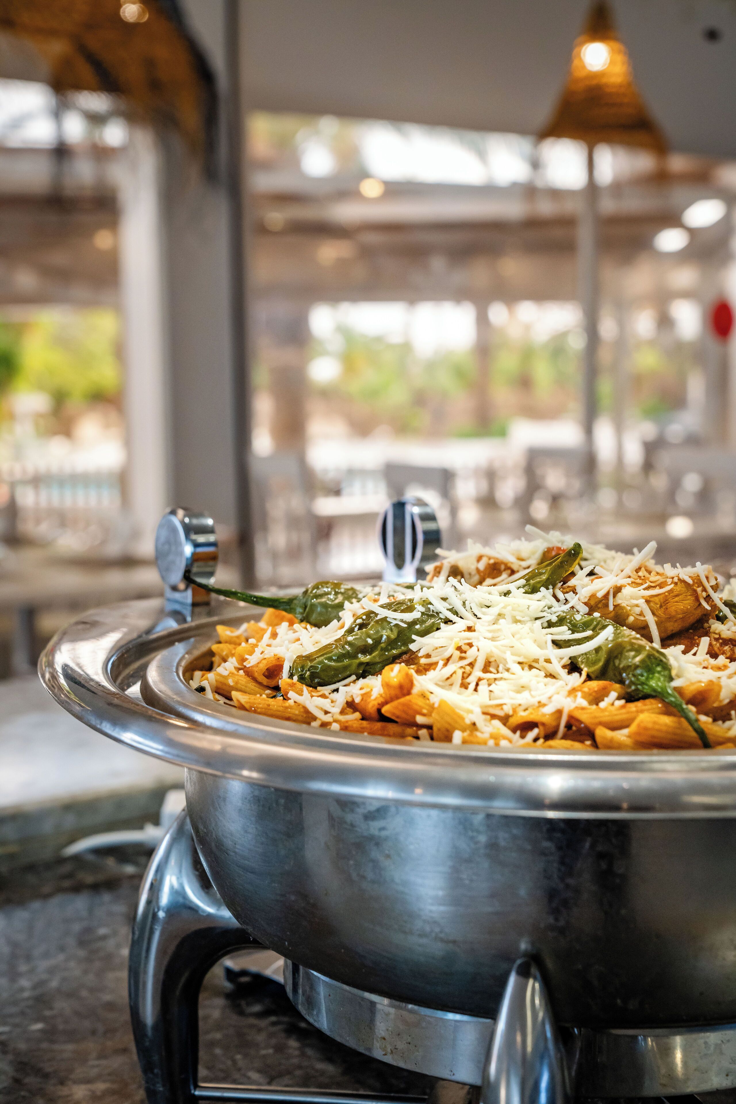 A metal serving dish with pasta and cheese, placed on a table in a well-lit indoor setting.
