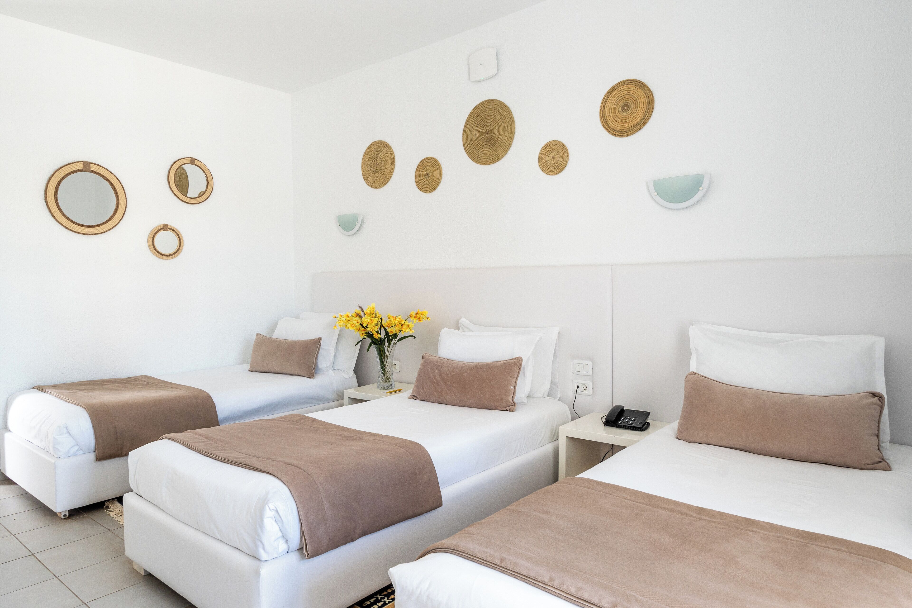 A hotel room with three beds, a bedside table with a phone, and decorative wall art.