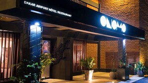Exterior del RESTAURANTE HOTEL DAKAR AIRPORT, con un letrero llamativo, zona de estar al aire libre y entrada bien iluminada.