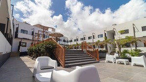 Un espacio exterior moderno con una escalera, sillas blancas y plantas en macetas.