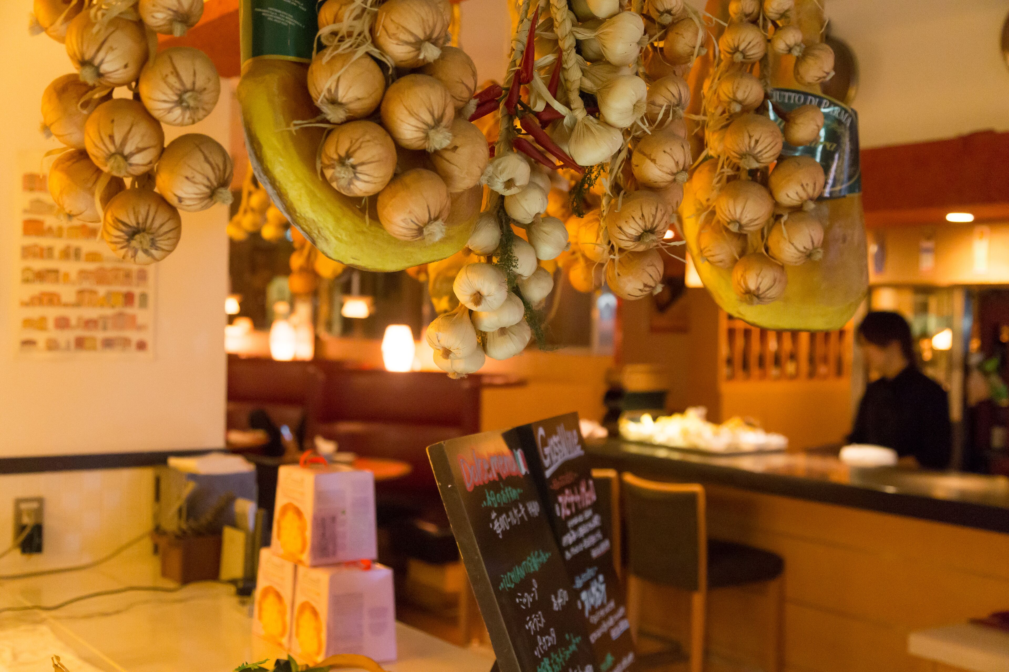 A restaurant interior with hanging garlic bulbs, a chalkboard menu, and a bar area.