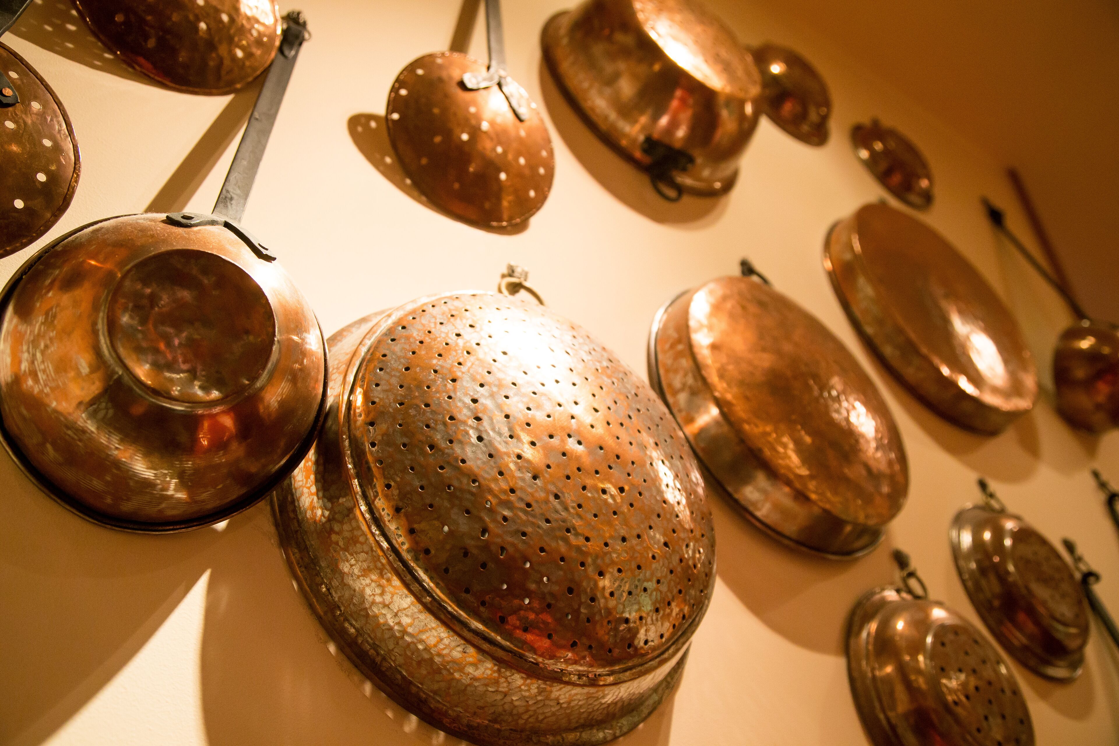 A collection of copper kitchen utensils hanging on a wall.