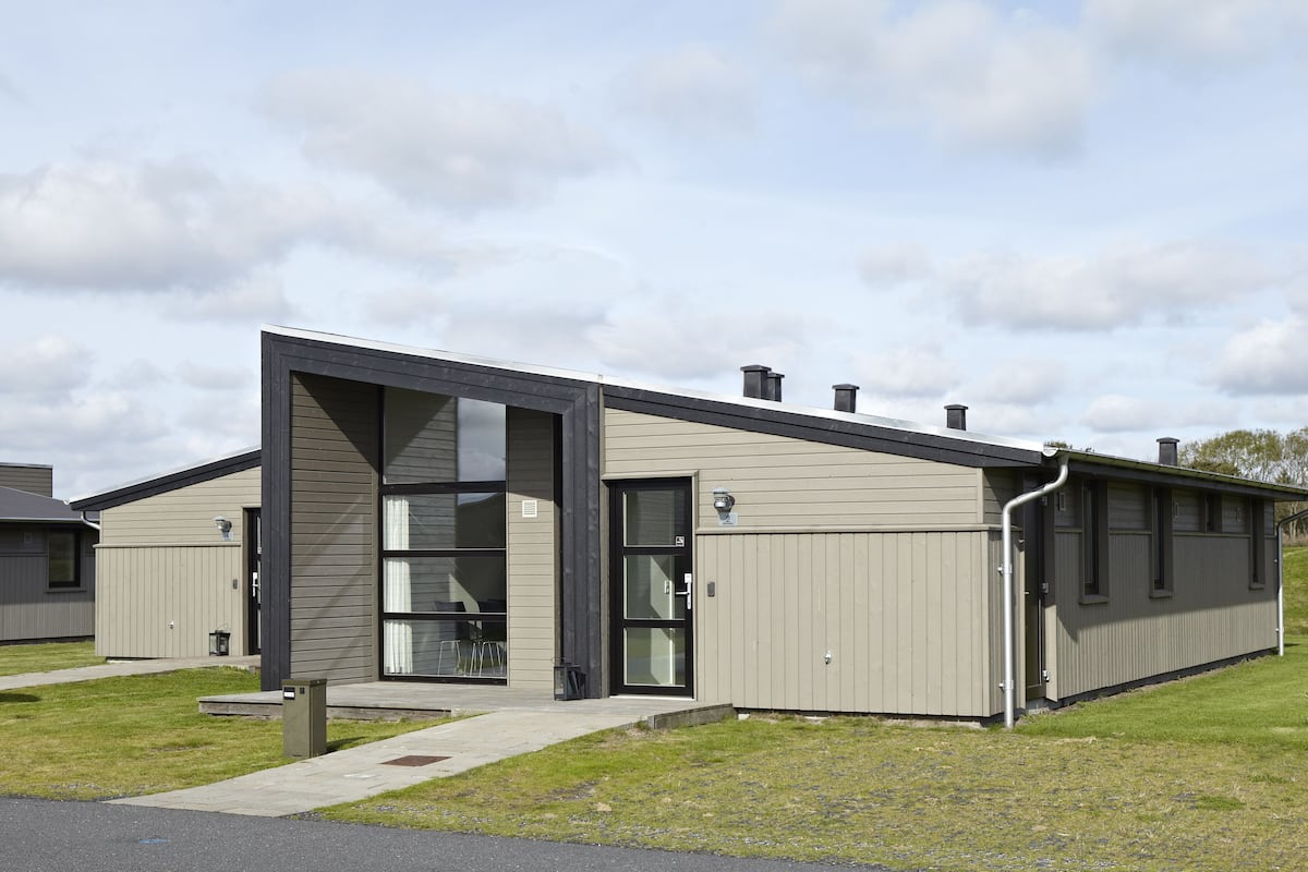 A modern building with a large glass door, a small attached structure, and a grassy area in front.