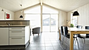 A modern kitchen with white cabinets, a large island, and a dining area with a wooden table and chairs. - Lalandia Resort Billund (Billund)