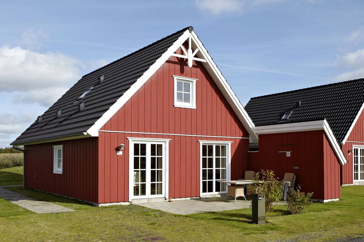 A red building with a sloped roof and white trim, featuring a large door and windows.