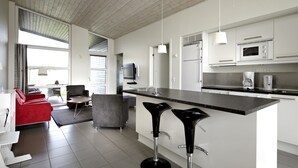 A modern kitchen with a central island, bar stools, a dining area with a red sofa, and a television. - Lalandia Resort Billund (Billund)
