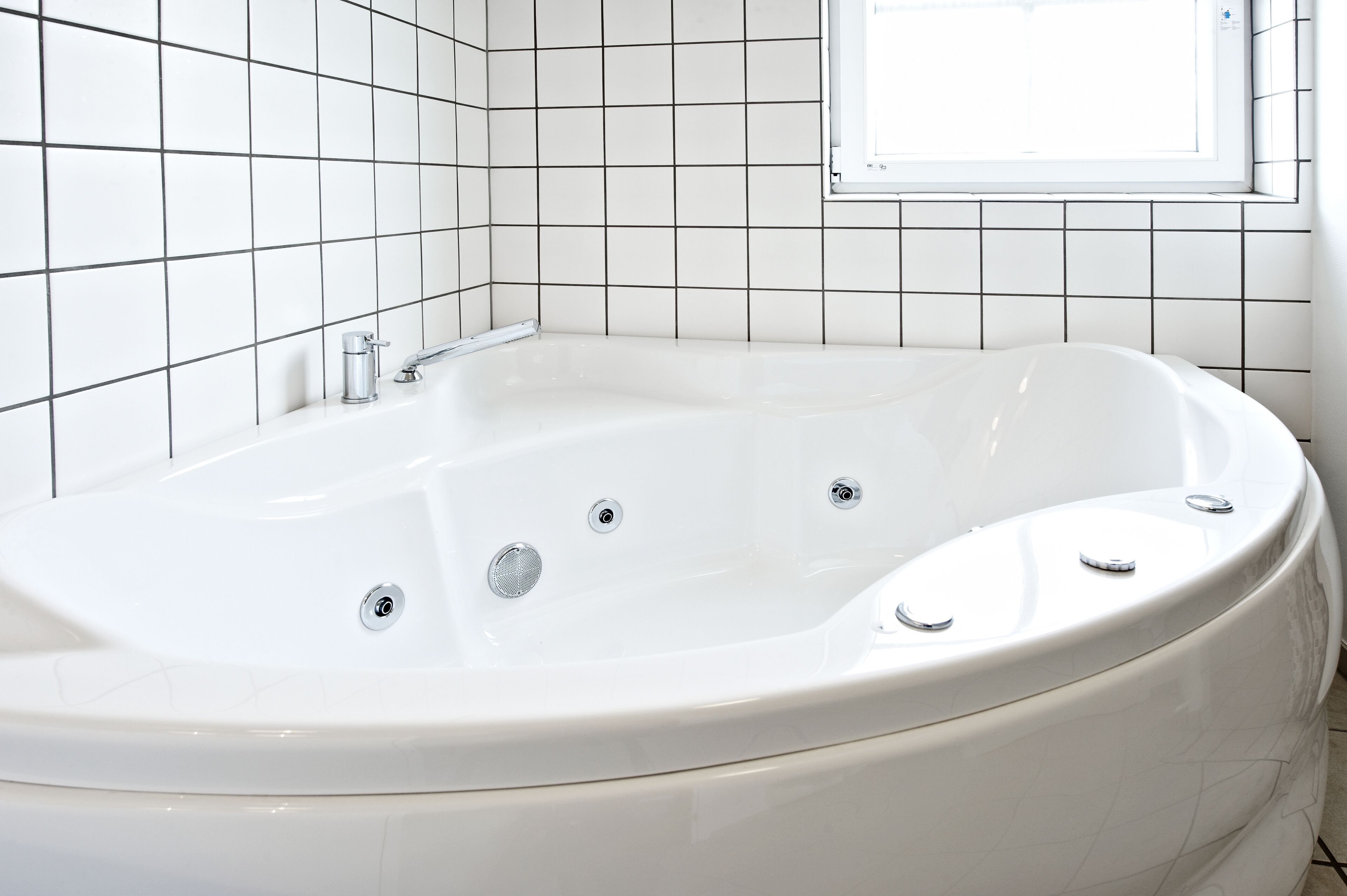 A white bathtub with three faucets and a window above it.