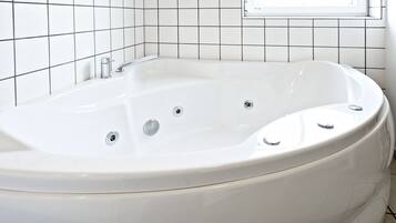 A white bathtub with three faucets and a window above it.
