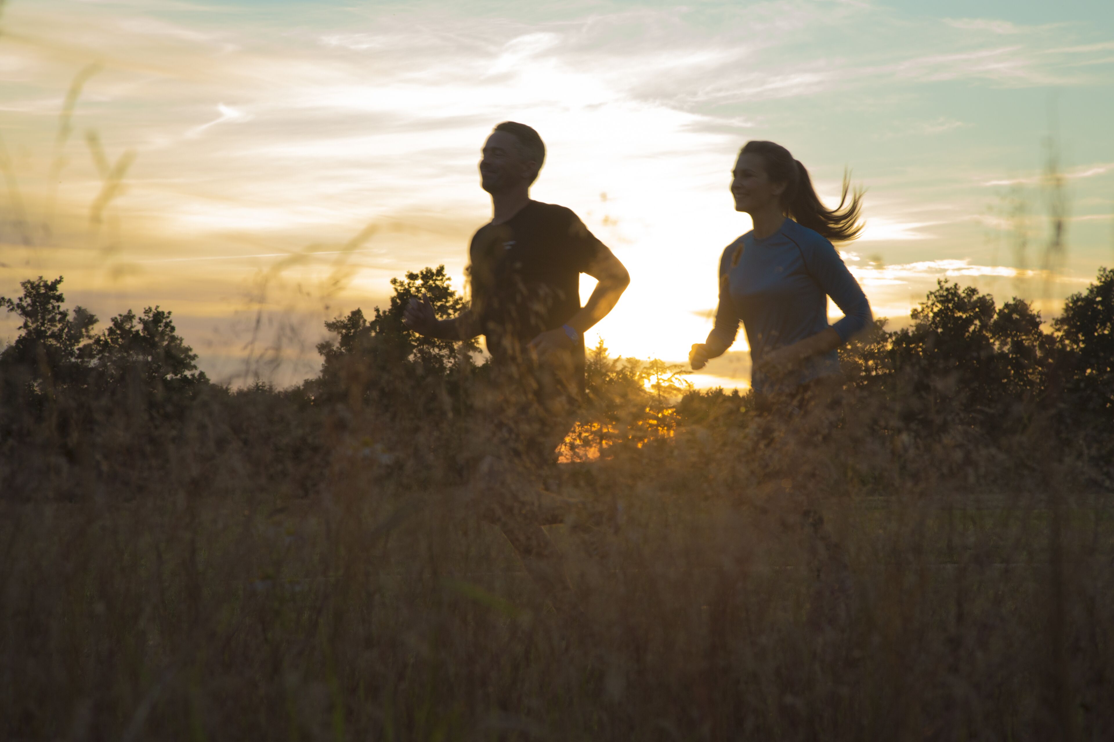 Two people jogging in a field with a sunset in the background.