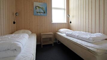 Ett rum med två sängar, ett litet träbord vid sängen, en tavla på väggen och ett fönster som släpper in naturligt ljus.