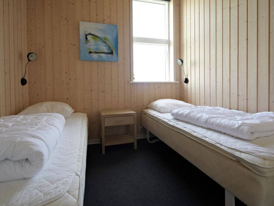 Una habitación con dos camas, una mesita de noche de madera, un cuadro en la pared y una ventana que deja entrar luz natural.