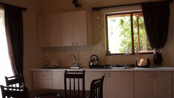 A kitchen with wooden cabinets, a window with curtains, a kettle, and a stove. - Forest Creek Lodge & Spa (Mashishing)