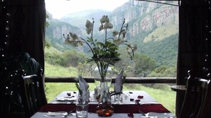 A dining table set for two with a view of a mountainous landscape.