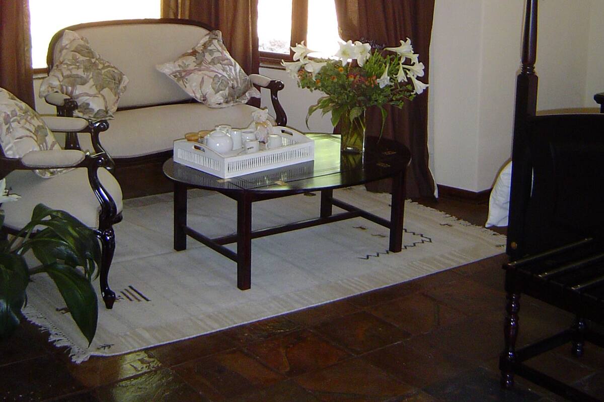 A living room with a sofa, a coffee table, and a vase of flowers. There are curtains on the windows and a plant on the floor.