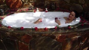 A stone-walled bathtub filled with water and rose petals, with a person using a smartphone. - Forest Creek Lodge & Spa (Mashishing)