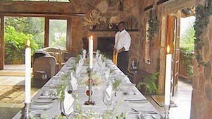 A long dining table set with white tablecloth, candles, and floral centerpieces in a room with stone walls and large windows. - Forest Creek Lodge & Spa (Mashishing)