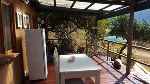 A covered outdoor area with a table and chairs, a refrigerator, and a view of the beach.