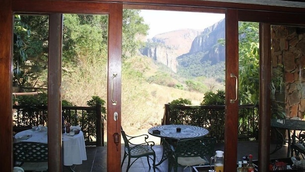 A dining area with a table and chairs, a view of a canyon, and a stone wall. - Forest Creek Lodge & Spa (Mashishing)