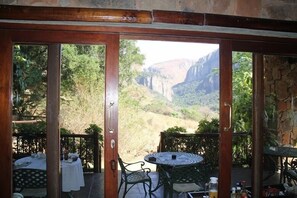 A dining area with a table and chairs, a view of a canyon, and a stone wall. - Forest Creek Lodge & Spa (Mashishing)