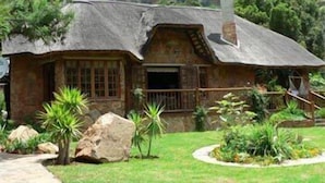 A rustic stone house with a thatched roof, surrounded by lush greenery and a stone pathway. - Forest Creek Lodge & Spa (Mashishing)