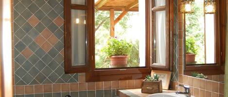 A bathroom with a wooden ceiling, a window with a view of greenery, a sink, and two toilets.