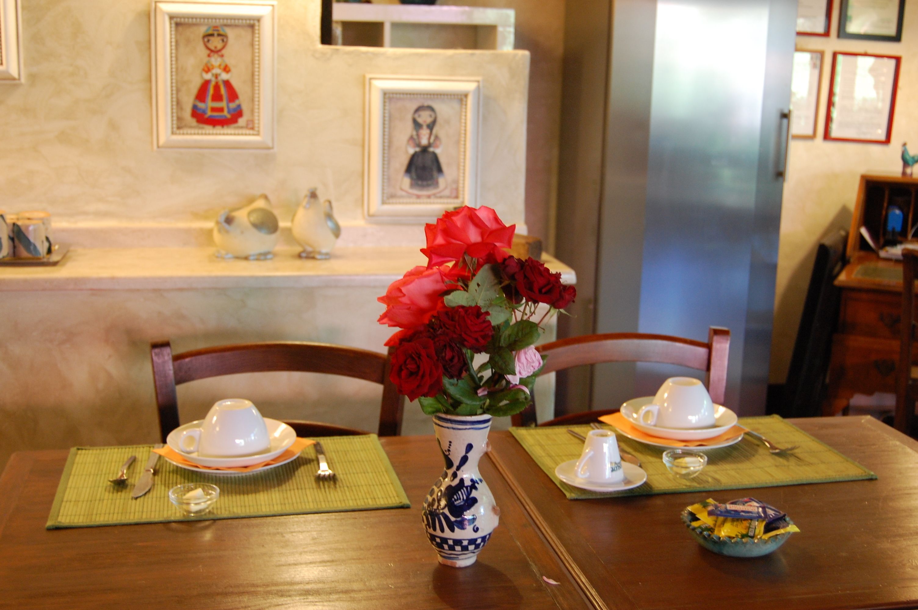 A dining table with a vase of red roses, white cups, and a bowl of snacks.