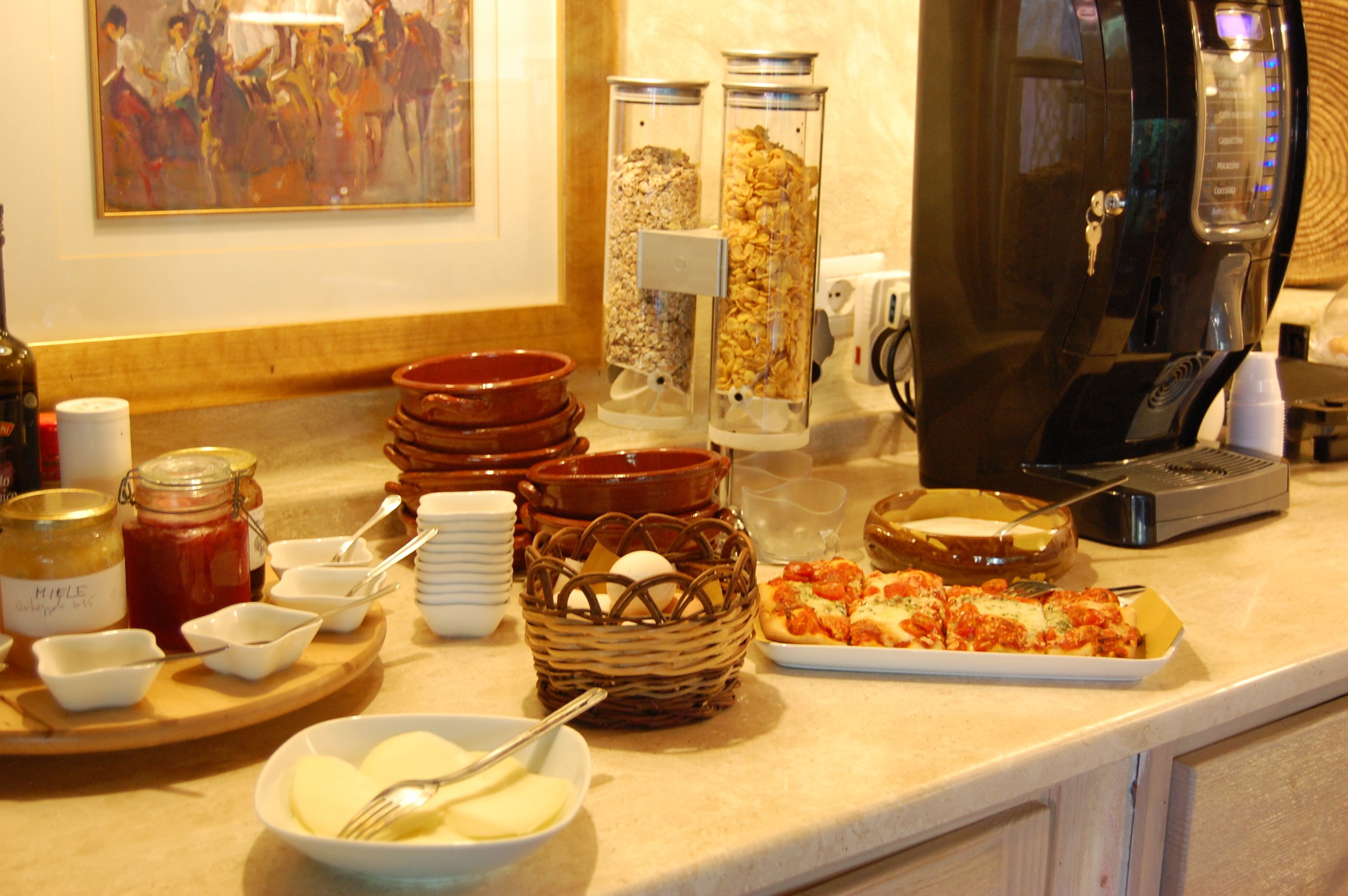 A buffet setup with various food items, including jars of condiments, a basket with bread, and a plate of pizza.
