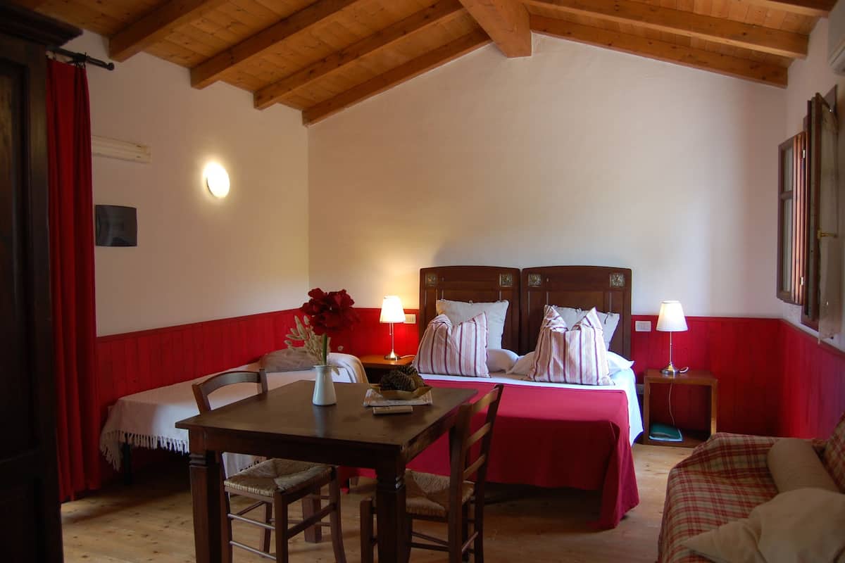 Ein Zimmer mit Holzboden, einem Bett mit weißer Bettwäsche, einem Tisch und Stühlen sowie einer roten Wand.