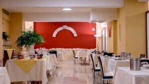 A restaurant with multiple tables set for dining, a potted plant, and a red accent wall. - Hotel San Michele (Milazzo)
