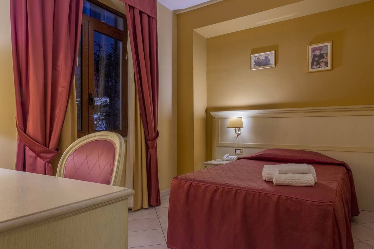Une chambre d’hôtel comprenant un lit, un bureau, une chaise, une table de chevet et deux tableaux encadrés accrochés au mur.
