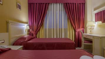 Habitació d'hotel amb dos llits, una taula de treball, una cadira i una finestra amb cortines.