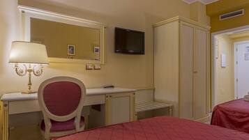 Ein Hotelzimmer mit Schreibtisch, Stuhl, zwei Betten, einem Fernseher und einem Kleiderschrank.