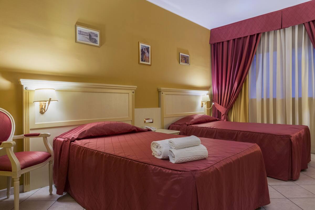Une chambre d’hôtel avec deux lits, une chaise, une table de chevet et une lampe fixée au mur.