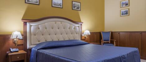 A hotel room with a large bed, two bedside tables, a chair, and three framed pictures on the wall.