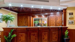 A reception desk with a wooden finish, a reception area, and potted plants. - Hotel San Michele (Milazzo)