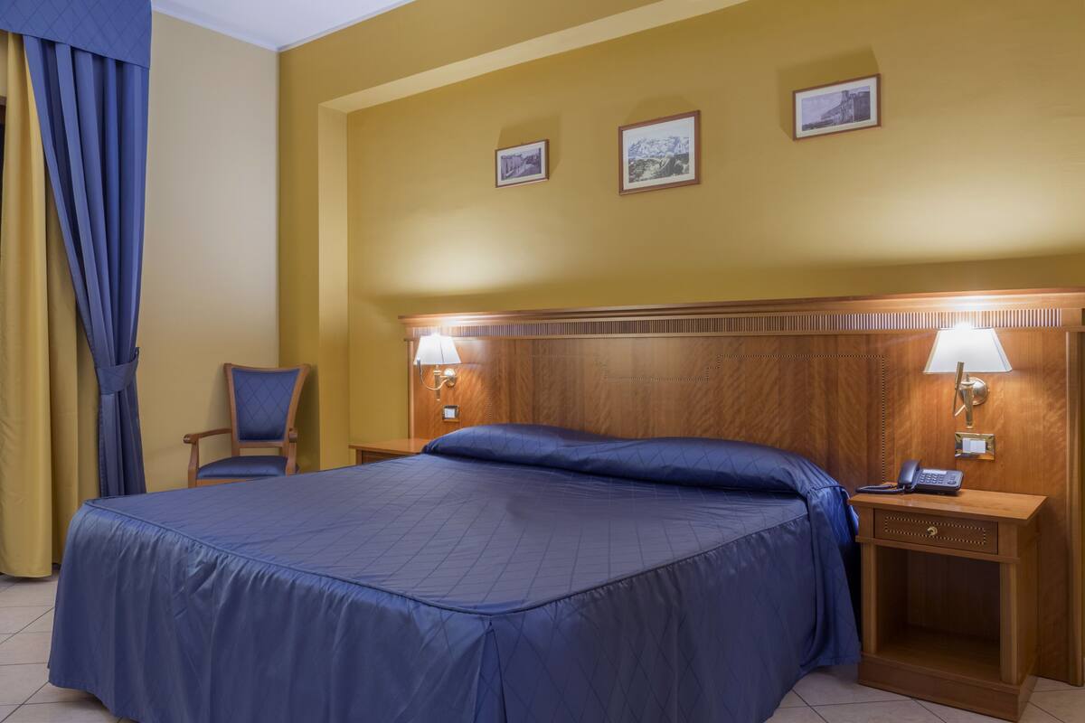 Une chambre d’hôtel avec un grand lit, deux lampes de chevet, une tête de lit en bois et une chaise.