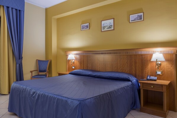 Una habitación de hotel con una cama grande, dos lámparas de noche, un cabecero de madera y una silla.