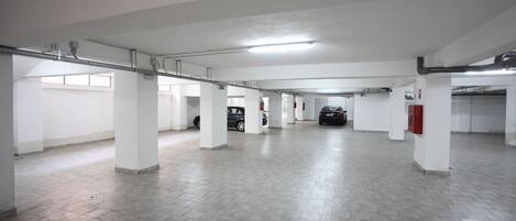 A spacious parking garage with white pillars, tiled floors, and fluorescent lighting.