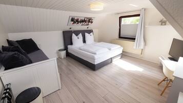 A bedroom with a bed, a desk, a chair, a radiator, a window with curtains, and a wall-mounted picture.
