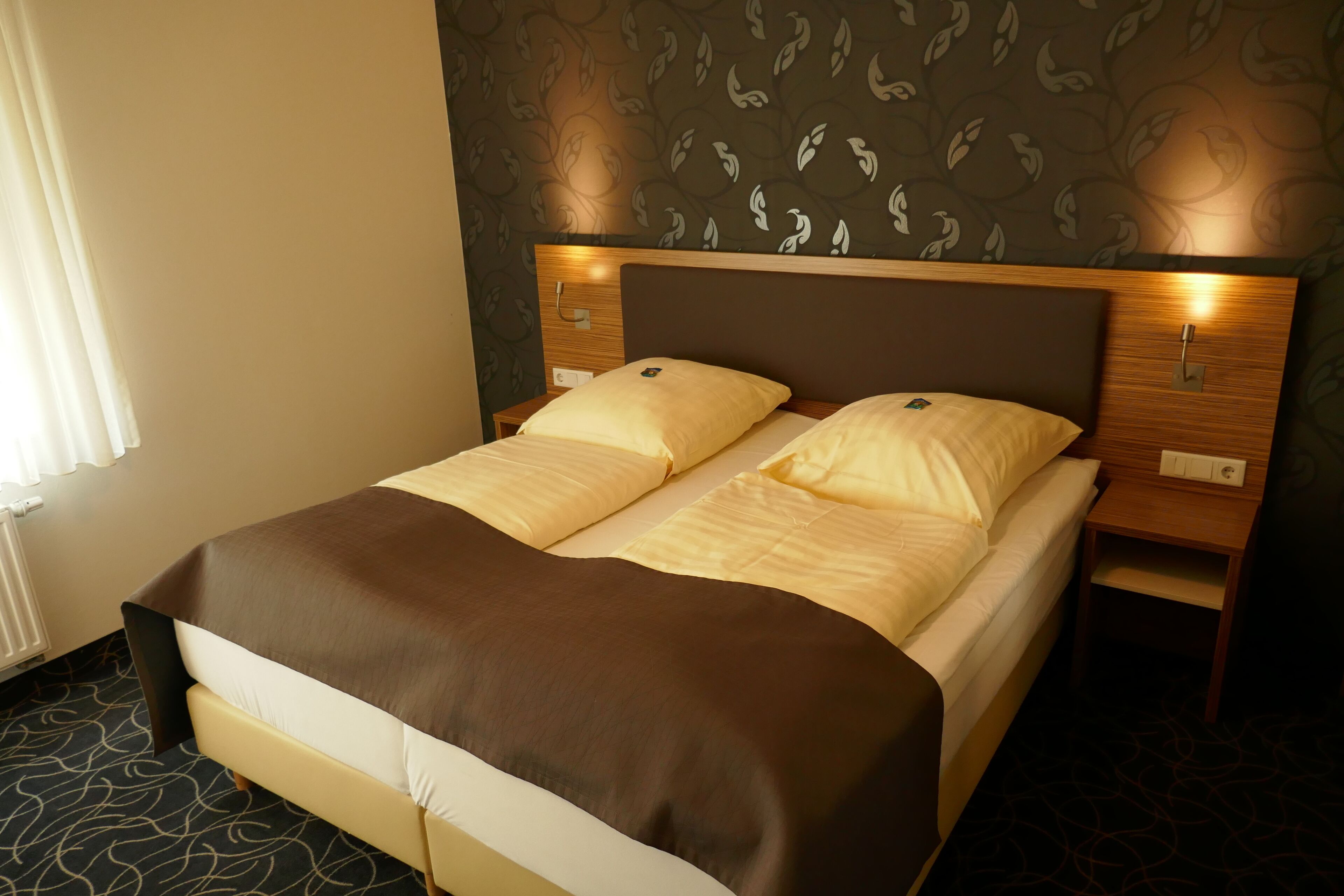 A hotel room with a large bed, two bedside tables, and a wall with a leaf pattern.